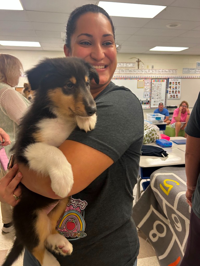 Teacher smiling while holding a puppy in a classroom