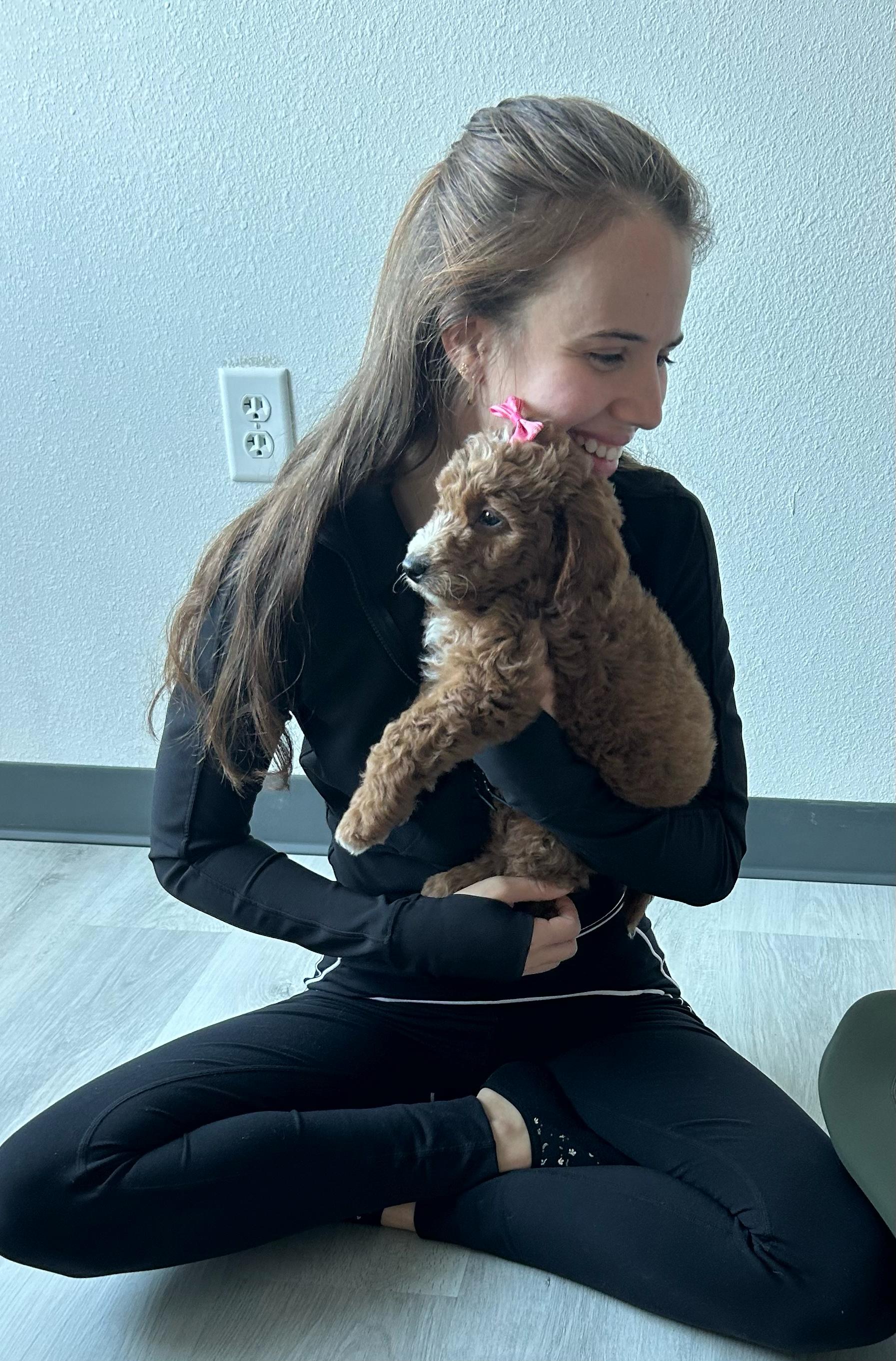 Woman cuddling golden Poodle puppy with pink bow
