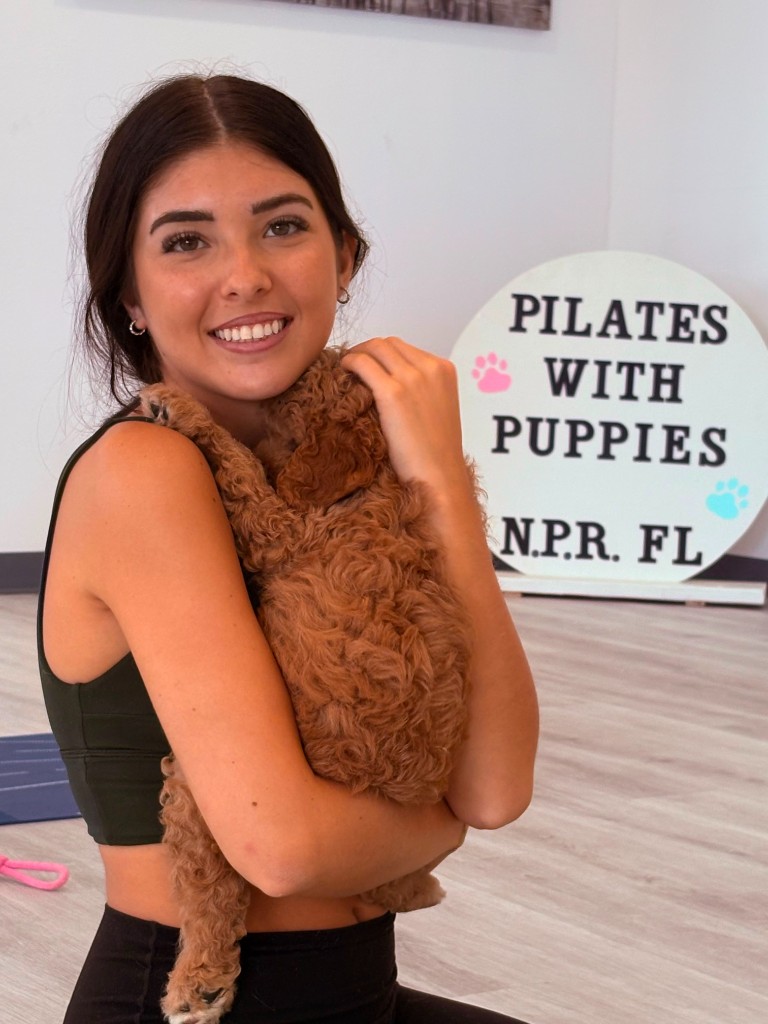 A guest cuddling a curly brown puppy during a Pilates with Puppies session in the New Port Richey studio.