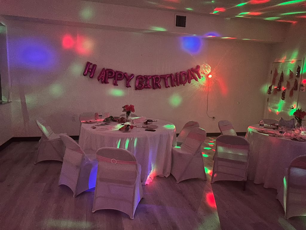 Studio set up for a birthday party with round tables, pink chair sashes, and a Happy Birthday banner